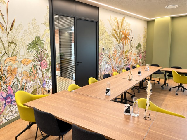 Salle de réunion de La Gravade : grande table en bois, chaises jaunes et tapisserie botanique
