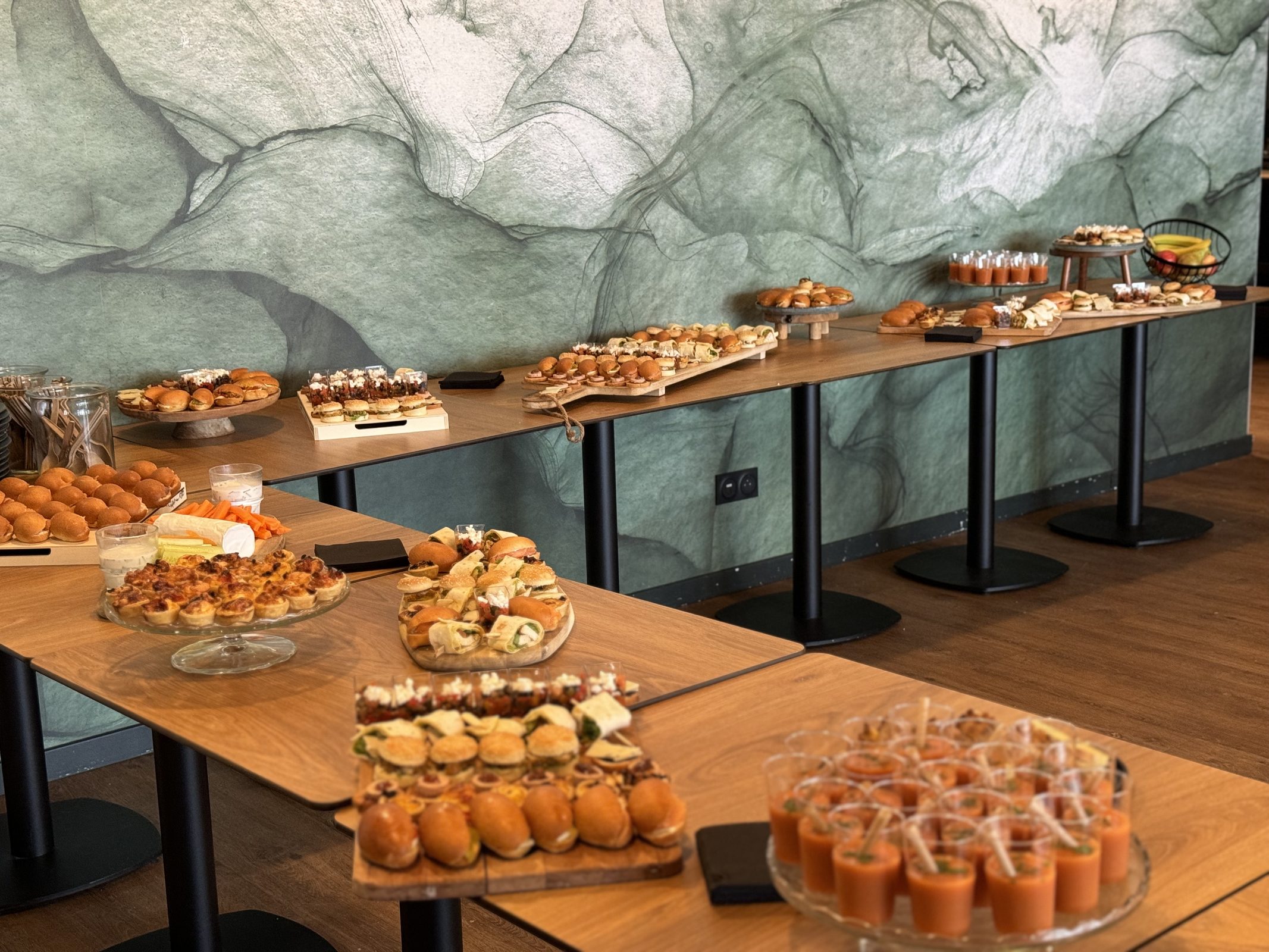 Buffet de petits fours et verrines dressé sur de longues tables devant un mur de marbre vert, La Gravade